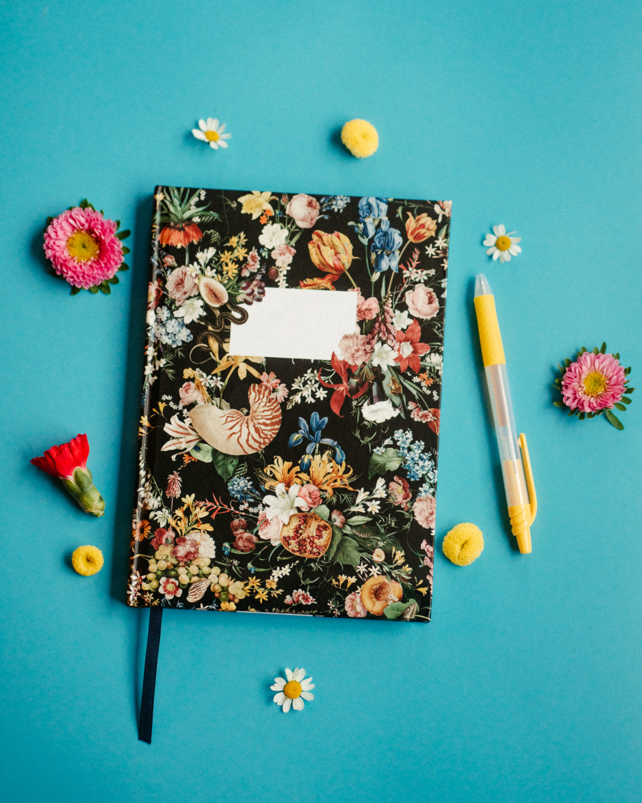 A floral planner and a pen sit on a blue background